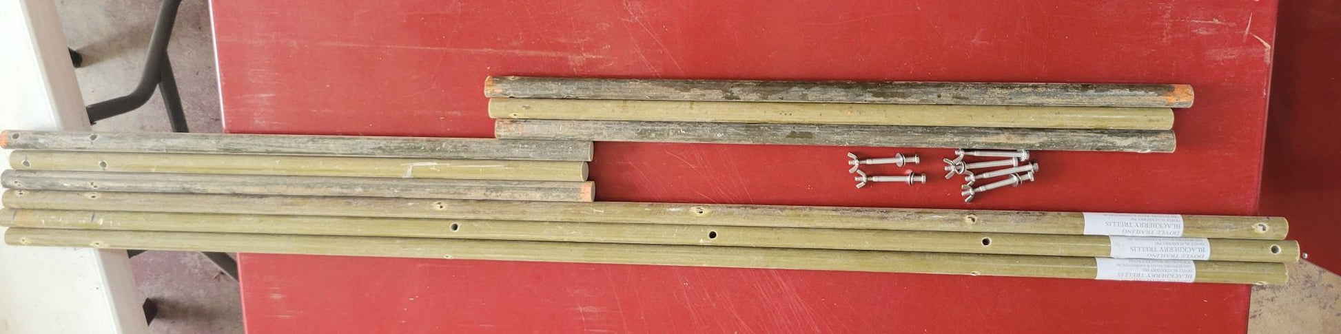Doyle Trailing Blackberry Shift Trellis components, including fiberglass rods and screws on a red surface.